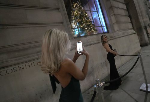 Two women dressed for a party take photos of each other outside a venue in London,  Friday, Dec. 17, 2021. 