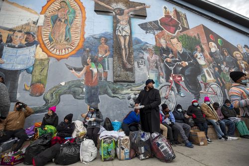 Migrants eat and wait for help while camping on a street in downtown El Paso, Texas, Sunday, Dec. 18, 2022. Texas border cities were preparing Sunday for a surge of as many as 5,000 new migrants a day across the U.S.-Mexico border as pandemic-era immigration restrictions expire this week, setting in motion plans for providing emergency housing, food and other essentials. (AP Photo/Andres Leighton)