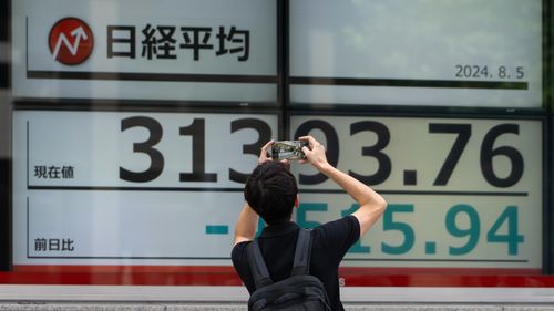 A pedestrian takes a photograph of monitors displaying the Nikkei 225 Stock Average figure outside a securities firm.