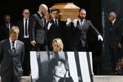 A person holds a portrait of Jane Birkin as pallbearers carry Jane Birkin's coffin after her funeral ceremony at the Saint-Roch church in Paris, Monday, July 24, 2023. Actor and singer Jane Birkin, who made France her home and charmed the country with her English grace, natural style and social activism, has died last week at age 76. (AP Photo/Thomas Padilla)