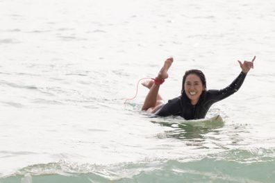 A Japanese female surfer smiles as she paddles along the shore.