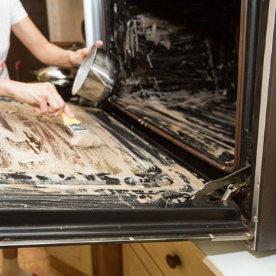 Person applying mixed baking soda onto surface of oven for effective and safe cleaning