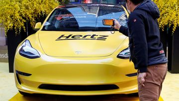 A man photographs a Hertz Tesla electric vehicle displayed during the Hertz Corporation IPO at the Nasdaq Market site in New York City on November 9, 2021. Hertz will sell off a third of its electric fleet, totaling roughly 20,000 vehicles.