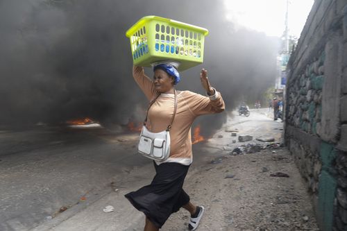 A woman runs past burning tires set by protesters against Haitian Prime Minister Ariel Henry in Port-au-Prince, Haiti, Monday, Feb. 5, 2024.