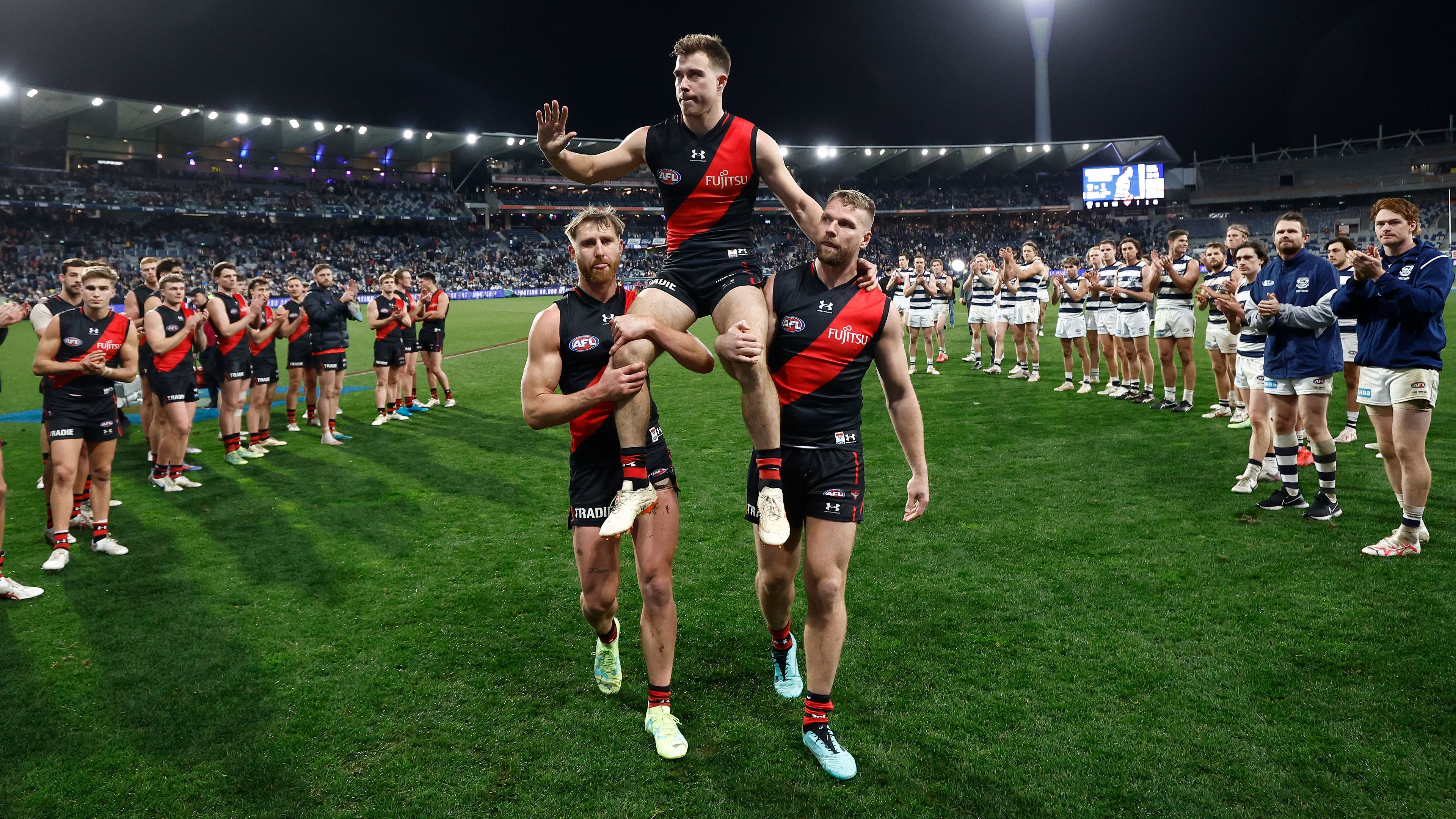 GEELONG, AUSTRALIA - JULY 15: Zach Merrett of the Bombers is chaired from the field after his 200th match by teammates Dyson Heppell (left) and Jake Stringer (right) during the 2023 AFL Round 18 match between the Geelong Cats and the Essendon Bombers at GMHBA Stadium on July 15, 2023 in Geelong, Australia. (Photo by Michael Willson/AFL Photos via Getty Images)