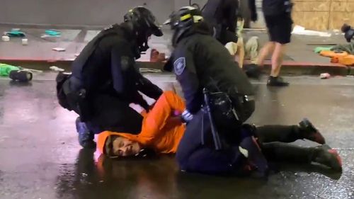 A suspected looter is pinned to the ground by two police officers, including one who uses his knee to hold the man to the ground.