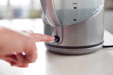 Close Up Of Woman Pressing Power Switch On Electric Kettle