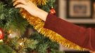 A woman decorates her tree with tinsel at Christmas 