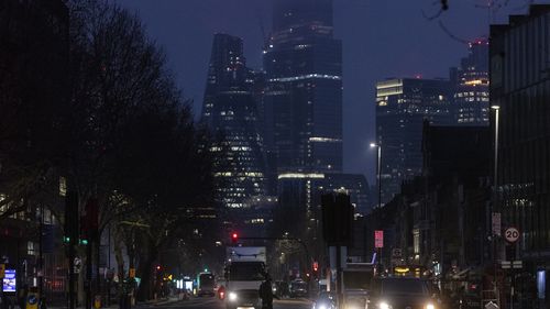 People walk across the road at dawn on Whitechapel Road on in London.