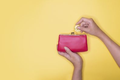 Hand taking out or inserting coin into purse on yellow background.