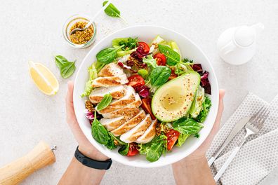 Grilled chicken meat and fresh vegetable salad of tomatoes, avocado, lettuce and spinach. Healthy and detox food concept. Ketogenic diet. Buddha bowl in hands on white background, top view