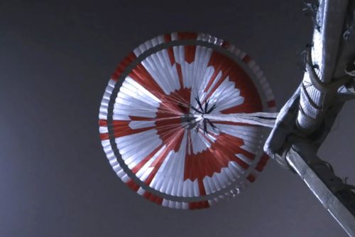 This image from video made available by NASA shows the parachute deployed during the descent of the Mars Perseverance rover as it approaches the surface of the planet on Thursday, Feb. 18, 2021. Systems engineer Ian Clark used a binary code to spell out Dare Mighty Things in the orange and white strips of the 70-foot (21-meter) parachute. He also included the GPS coordinates for the mission's headquarters at the Jet Propulsion Laboratory in Pasadena, Calif. (NASA/JPL-Caltech via AP)