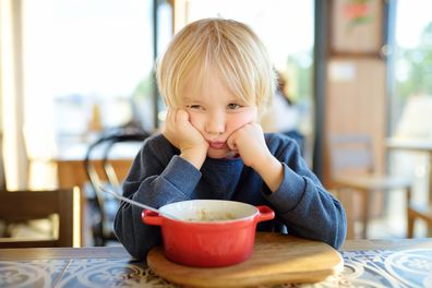 Little child sitting the table in cafe or restaurant and doesn't want to eat. Healthy food. Kids diet. Poor appetite. Grandmother upbringing.