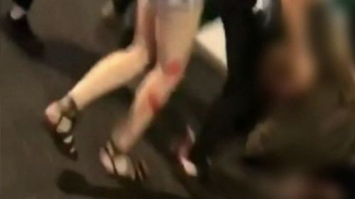 Blood is visible on the female attacker's legs as she continues to assault her victim.