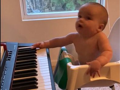 Baby moving his head along to music, sitting in front of a piano that his dad is playing.