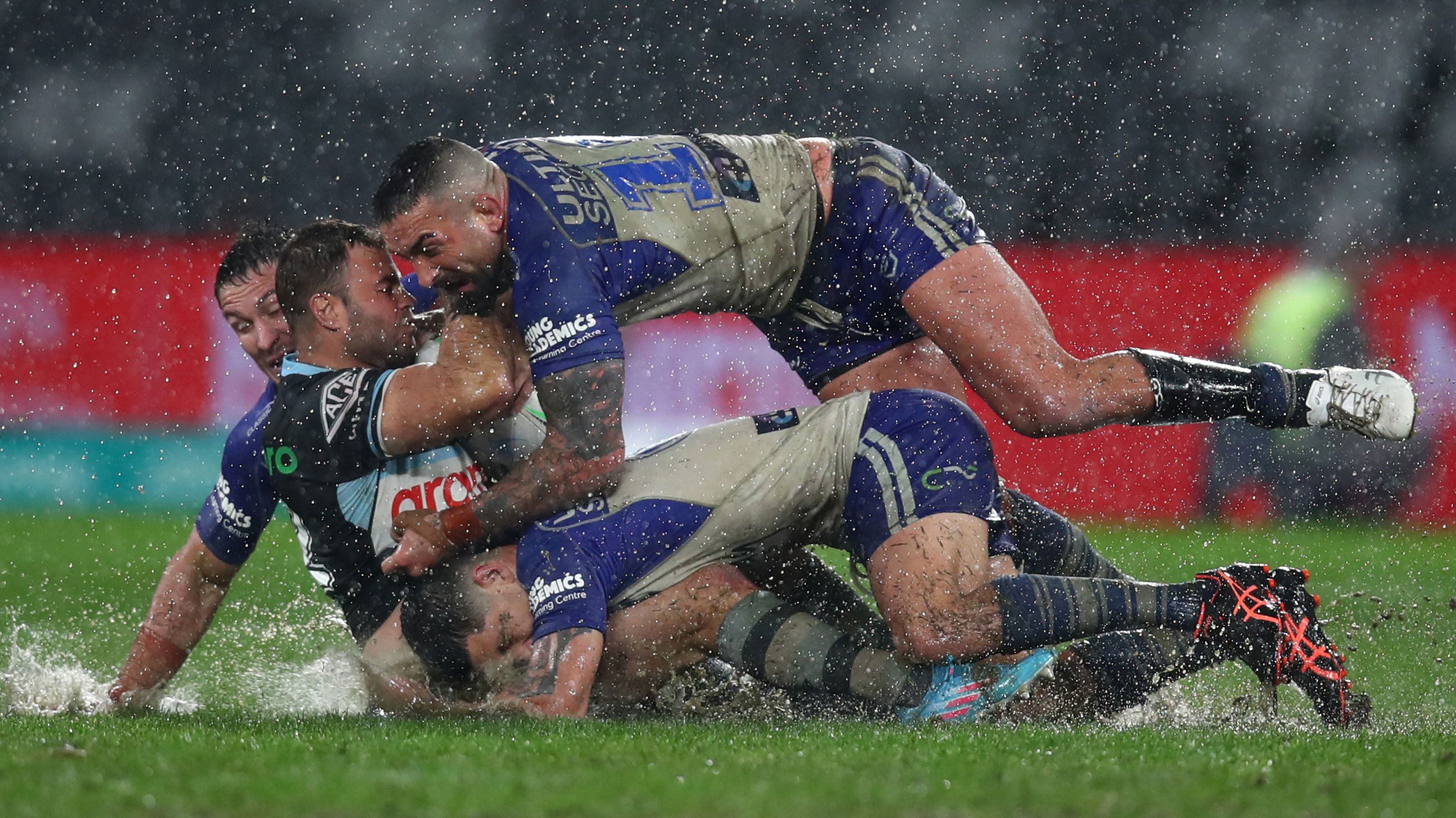Rain falls hard on the soggy surface as Wade Graham of the Sharks is tackled by Paul Vaughan of the Bulldogs during their round 16 NRL match.