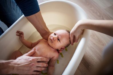 Unrecognizable parents giving a happy newborn baby a bath at home.