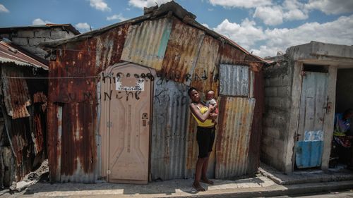 A woman poses for a photo outside her makeshift home built after gangs set her home on fire, in the Cite Soleil slum of Port-au-Prince, Haiti.