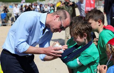 Prince William, the Duke of Cornwall, signs the cast of Felix Kanes, a member of Hollywell Bay Surf Life Saving Club, during a visit to Fistral Beach on May 9, 2024 in Newquay, Cornwall.