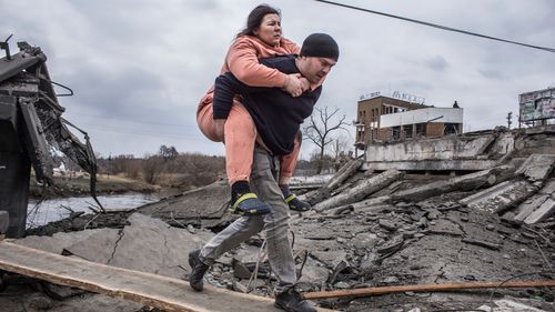 Un uomo tiene in braccio una donna mentre attraversano una strada improvvisata mentre fuggono dalla città di Irbin, in Ucraina.