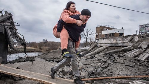 Мужчина держит женщину, когда они переходят импровизированную дорогу, убегая из города Ирбин, Украина.