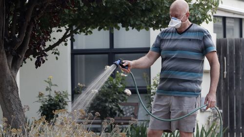 A resident waters his garden wearing a mask as smoke shrouds the Australian capital of Canberra, Australia, Thursday, Jan. 2, 2020. Australia deployed military ships and aircraft to help communities ravaged by apocalyptic wildfires that destroyed homes and sent thousands of residents and holidaymakers fleeing to the shoreline.