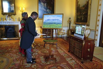 Queen Elizabeth appears on a screen via videolink from Windsor Castle, where she is in residence, during a virtual audience to receive the High Commissioner of Malawi, Dr. Thomas Bisika, centre, and his wife, at Buckingham Palace, London., Thursday, March 3, 2022. 