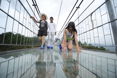 Tourists walk on a suspension bridge made of glass at the Shiniuzhai National Geological Park 