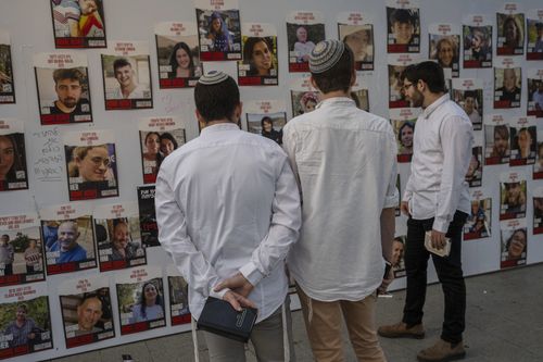 Israeli young men look at photos of Israelis missing and held captive in Gaza, displayed on a wall in Tel Aviv, on Friday, Oct. 20, 2023.  