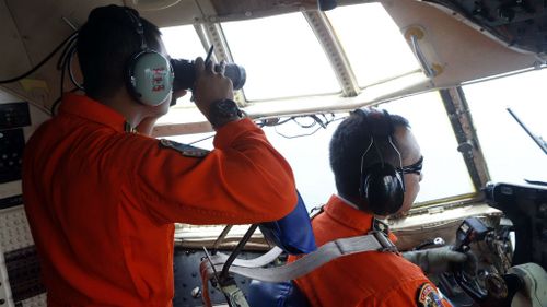 Indonesian Air Force members look out the cockpit windows of C-130 for the missing AirAsia jet. (AAP)