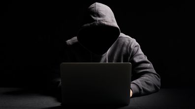 Hacker working on laptop in the dark - online scam - dark silhouette