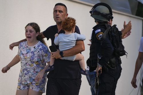 Israeli police officers evacuate a family from a site hit by a rocket fired from the Gaza Strip, in Ashkelon, southern Israel, Saturday, Oct. 7, 2023.  