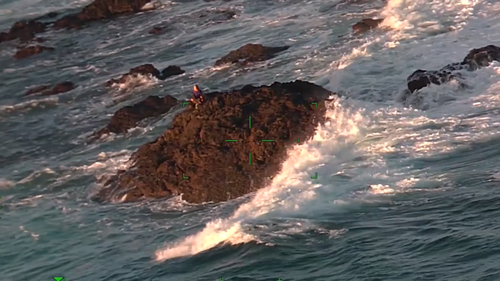 The 56-year-old ﻿was spotted squatting on top of the outcrop as waves crash around him. 
