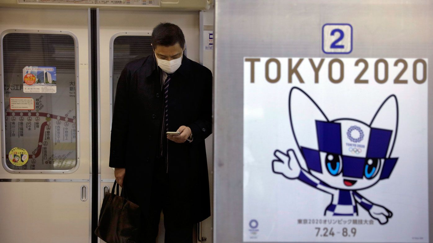 A poster promoting the Tokyo 2020 Olympics is posted next a train door as a commuter wearing a mask looks at his phone in a train