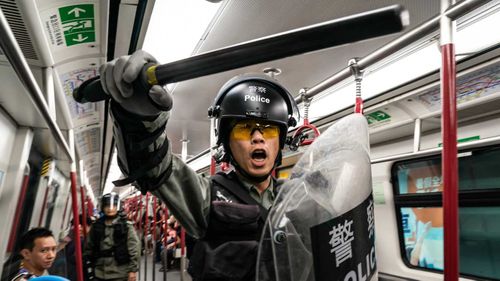 A Hong Kong police officer wields a heavy baton on a train.