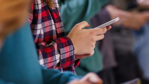Close-up group of teenagers using mobile phones in school corridor