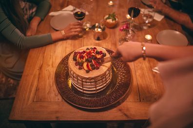 Woman cutting slices of gourmet mediterranean birthday cake with fruit at rustic dinner party