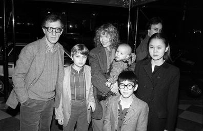 American comedian, actor, and film director Woody Allen (left) and his partner, actress Mia Farrow pose under an awning with their children, from left, Misha, Dylan (in Farrow's arms), Fletcher, and Soon Yi, New York, New York, 1986. Soon-Yi later married Allen. The man in background is unidentified. 