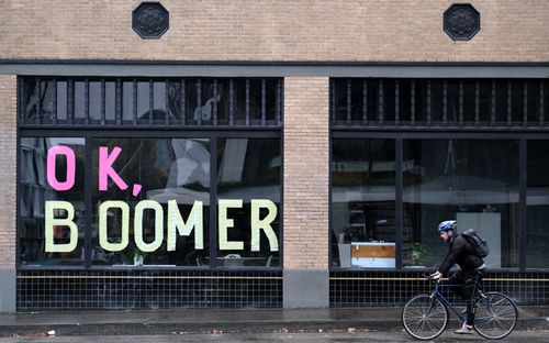 A man bikes past sticky notes arranged to display the phrase "OK Boomer" in a window of a business in Portland, Oregon.