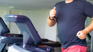 smiling full male runs on a treadmill in a gym. concept of weight loss and sport. side view