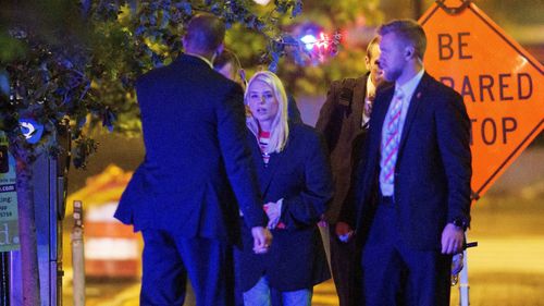 Attorney General Pam Bondi, centre, walks to her car as law enforcement work the scene.