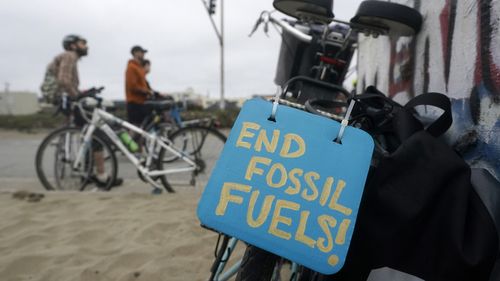 A sign reading "End Fossil Fuels" hangs on the back of a bicycle
