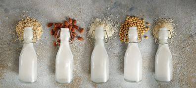 Bottles with different vegan milk and the ingredients like soy, nuts and cereals lying on a rough stone background, panoramic format, top view from above, selected focus