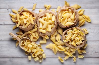 Assortment of raw pasta: penne, shells, rigatoni, fusilli and penne on wooden background, top view.
