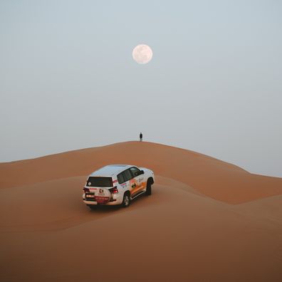 Person looking at full moon with car in background in desert