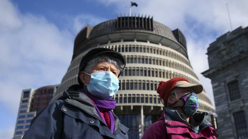 Two women pose in front of the Beehive while wearing face masks ahead of a COVID-19 Alert Level announcement on August 14, 2020 in Wellington, New Zealand.