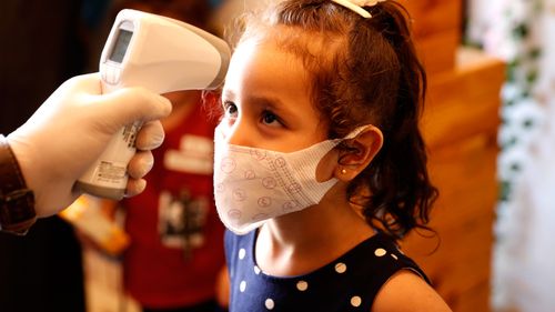 A girl wearing a mask has her body temperature checked while she arrives with her family at a beach side cafe in Gaza City
