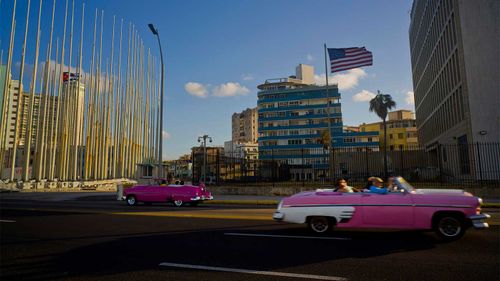 Old-school convertibles drive past the US embassy in Cuba.