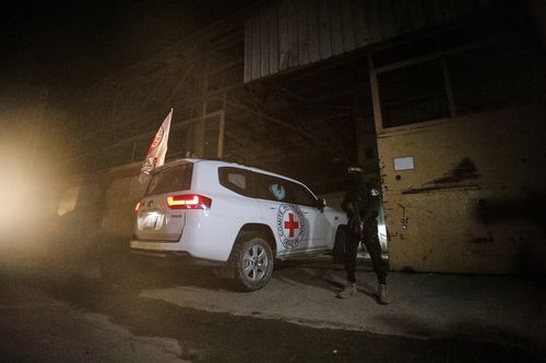 A gunman wearing the uniform of the al-Qassam Brigades, the military wing of Hamas, stands guard as Red Cross vehicles enter a warehouse allegedly to collect coffins containing the bodies of four deceased hostages, in Gaza.