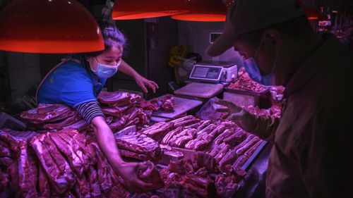 A Chinese meat vendor wears a protective mask as she serves a customer at her stall at a food market